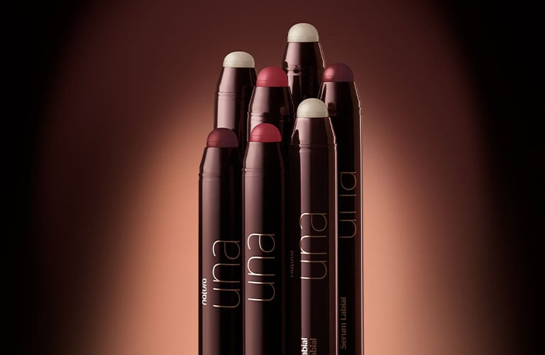 Foto con fondo degradado en tonos marrones. En el centro, varios sérums labiales de color marrón oscuro con diferentes puntas visibles en tonos claros y rojizos.